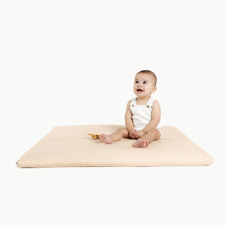 Baby sitting on the square petal cream vegan leather padded play mat with a wooden toy