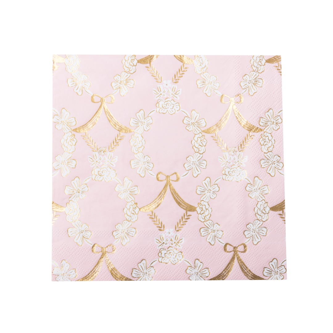 A stack of pink paper napkins featuring a repeating pattern of white cherry blossoms and gold bow motifs, shown on a clean white background.