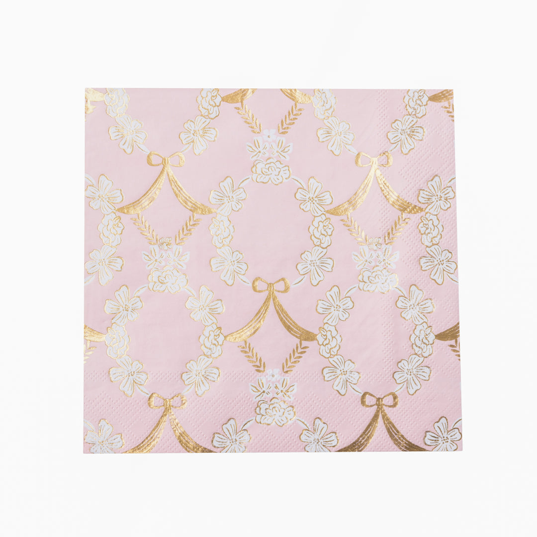 A stack of pink paper napkins featuring a repeating pattern of white cherry blossoms and gold bow motifs, shown on a clean white background.
