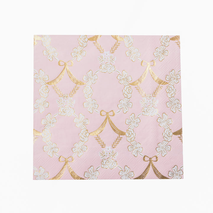 A stack of pink paper napkins featuring a repeating pattern of white cherry blossoms and gold bow motifs, shown on a clean white background.