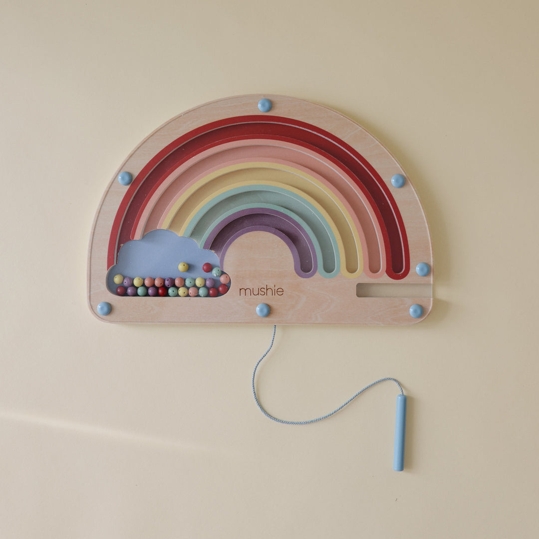 Child guiding beads on the Mushie wooden magnetic rainbow maze