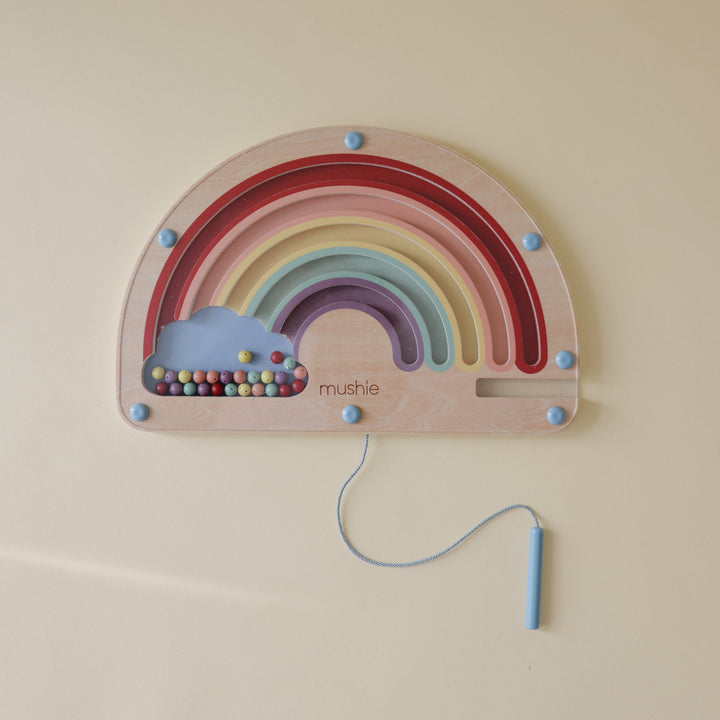 Child guiding beads on the Mushie wooden magnetic rainbow maze