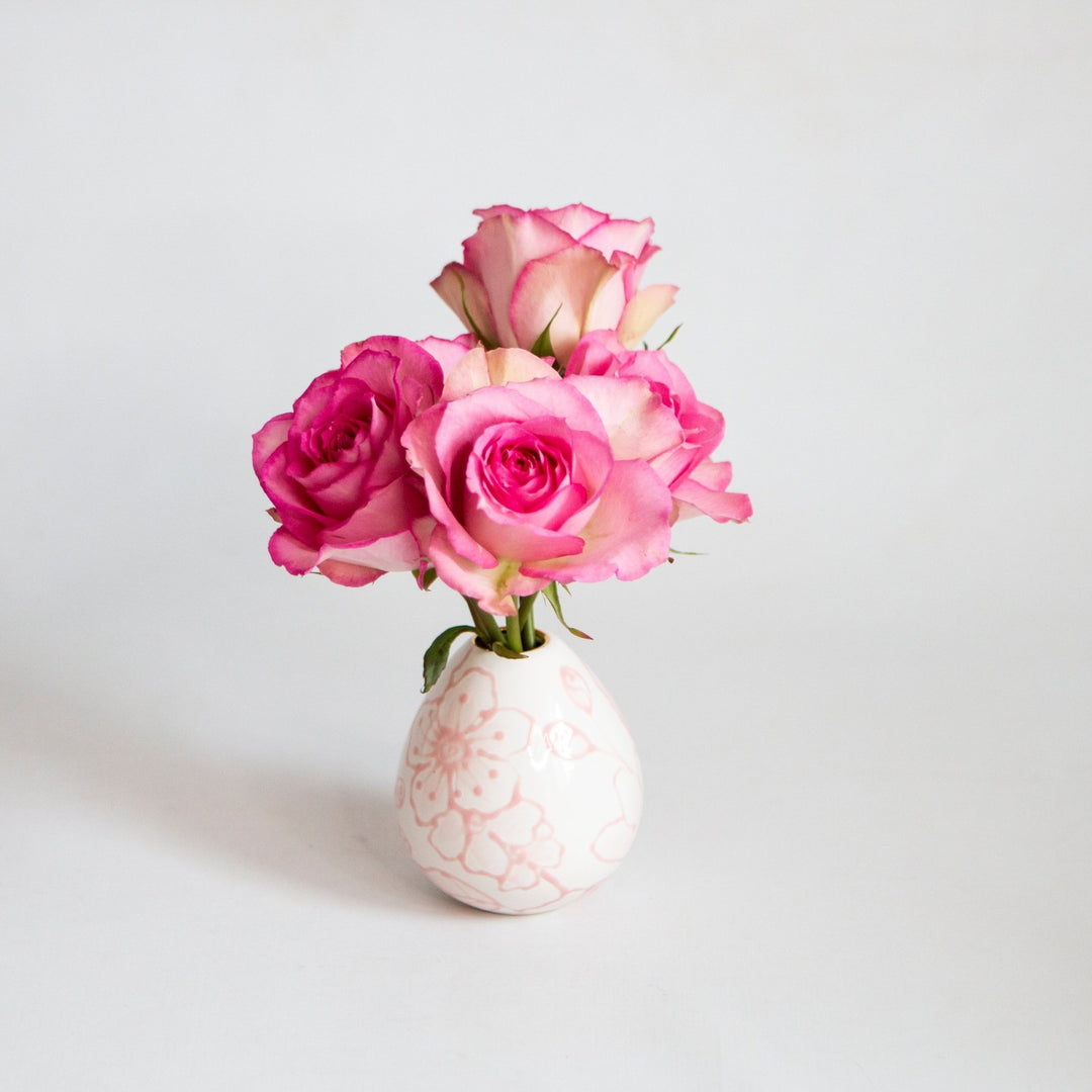 Small pink outlined floral bud vase filled with pink and cream garden roses on a light gray backdrop