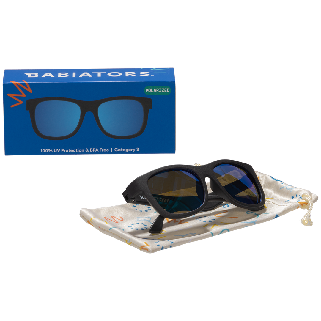 Black polarized aviator kids sunglasses folded on a printed storage pouch beside the Babiators box.