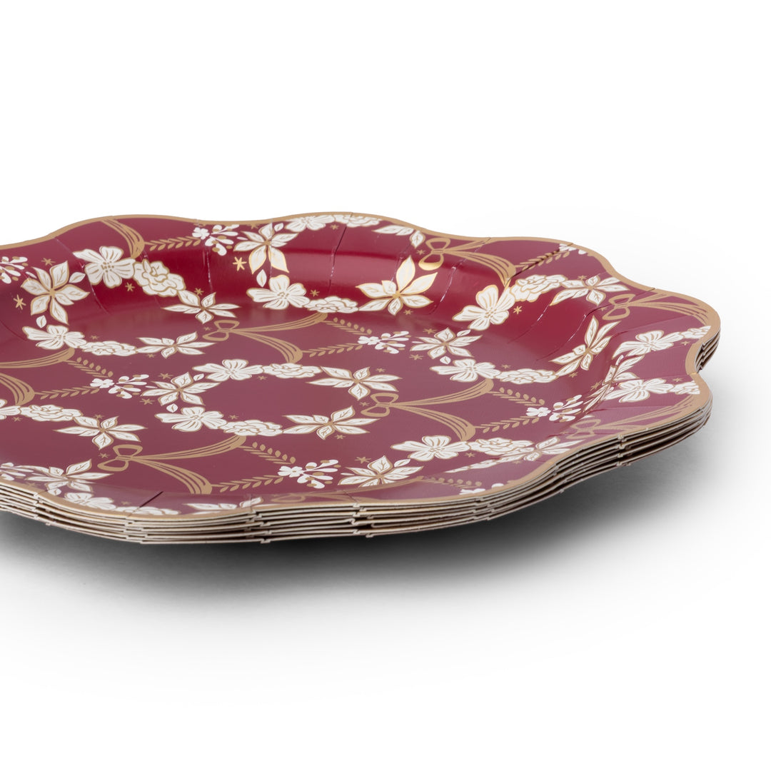 A stack of scalloped paper plates in a deep red color, decorated with a white floral wreath pattern and gold accents, shown on a white background.