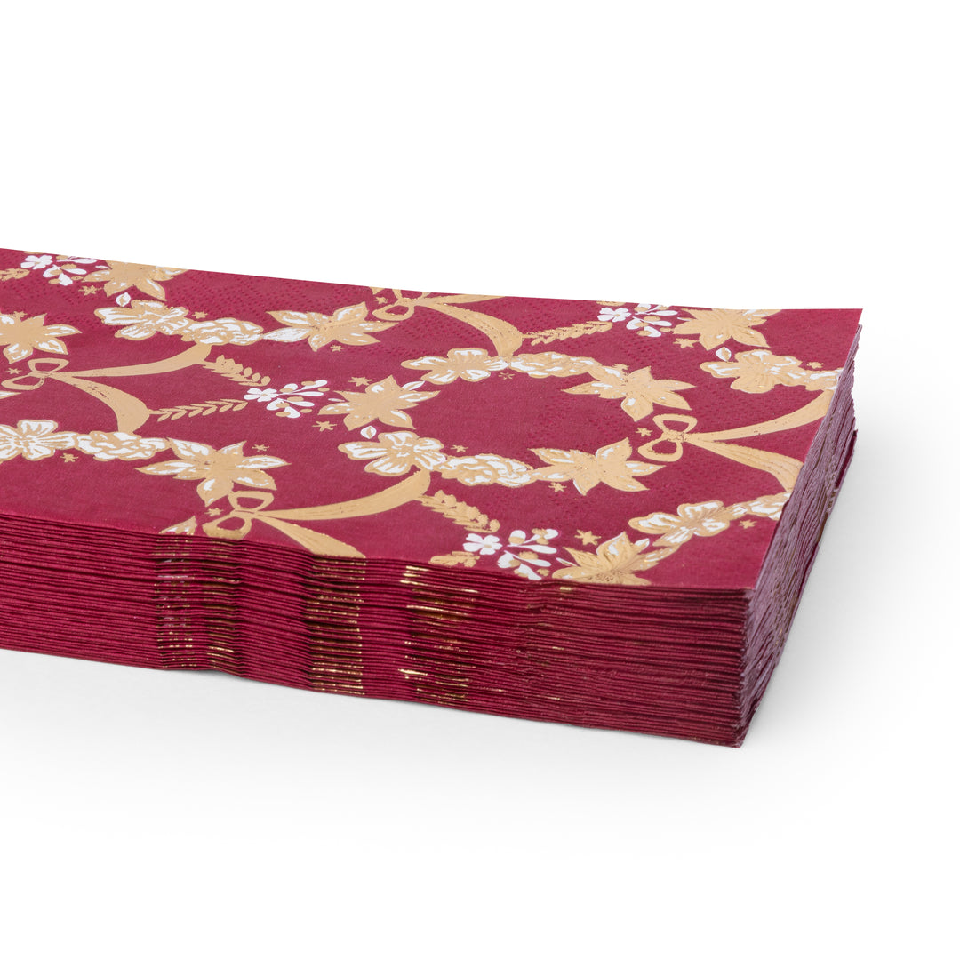 A stack of deep red paper napkins featuring a gold floral and vine pattern, with some white floral accents, shown on a clean white background.