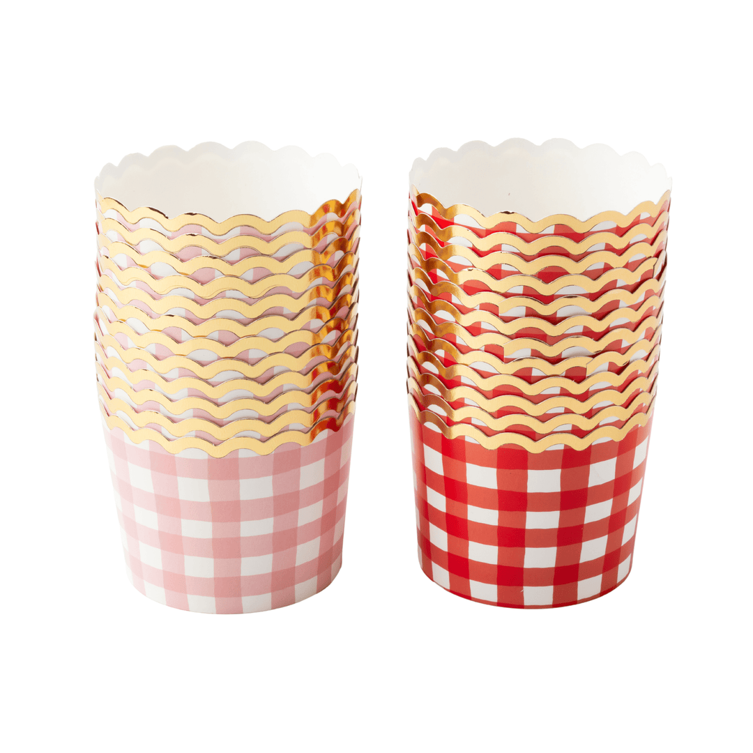 Two stacks of scalloped paper cupcake or treat cups on a white background. One g has a pink and white gingham pattern with a gold wavy metallic top, and the other has a red and white gingham pattern with a gold wavy metallic top.