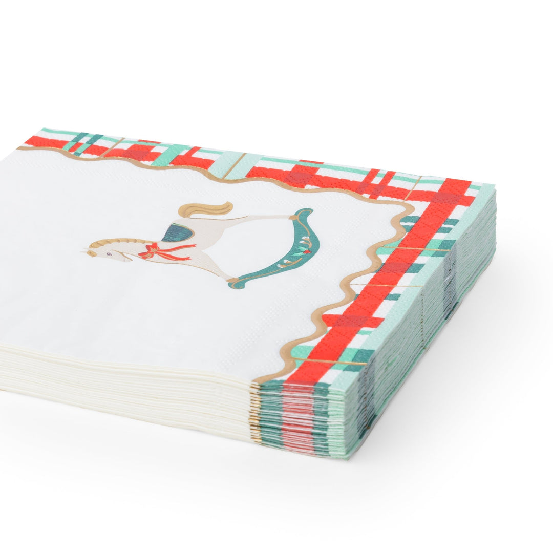 A stack of white paper napkins featuring a vintage-style rocking horse illustration and a decorative border with red, teal, and gold details, shown on a clean white background.