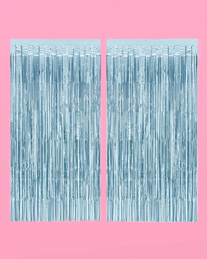 Two light blue foil fringe curtain panels hung side by side on a pink background
