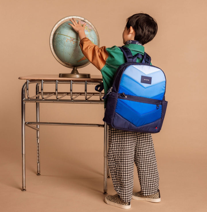 Boy at a vintage desk spinning a globe while wearing the Blue Chevron STATE Kane backpack