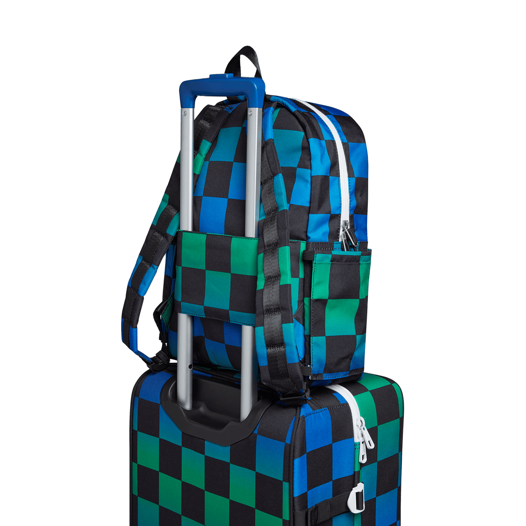 Blue Checkerboard Kane backpack slid over a rolling suitcase handle with its luggage sleeve
