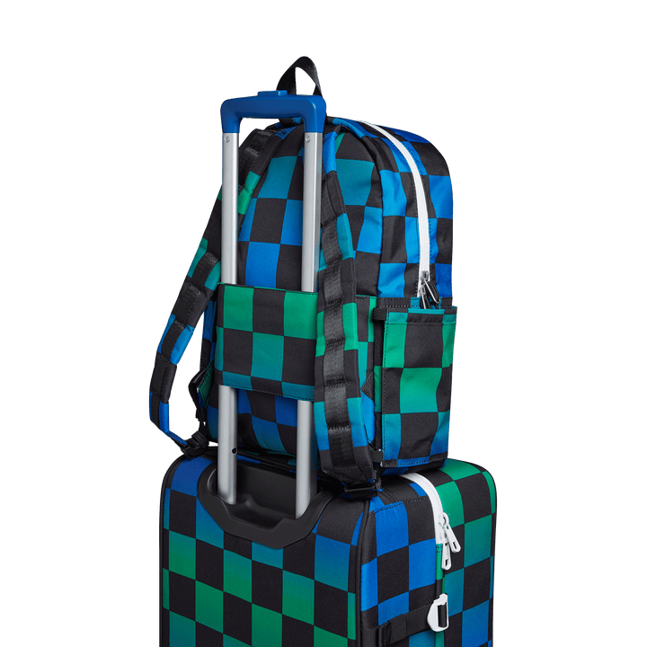Blue Checkerboard Kane backpack slid over a rolling suitcase handle with its luggage sleeve