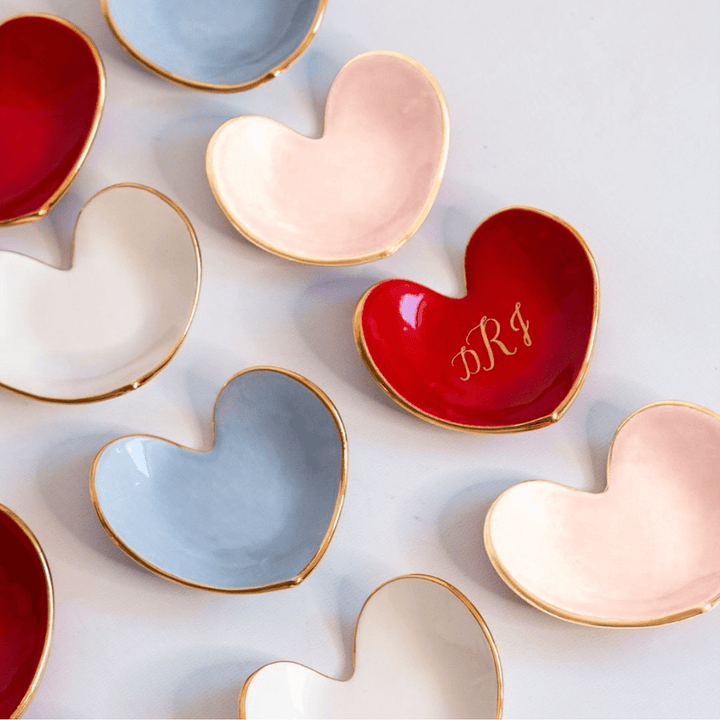 Assorted heart ring dishes in red, blush, light blue, and white, one red dish with a gold monogram