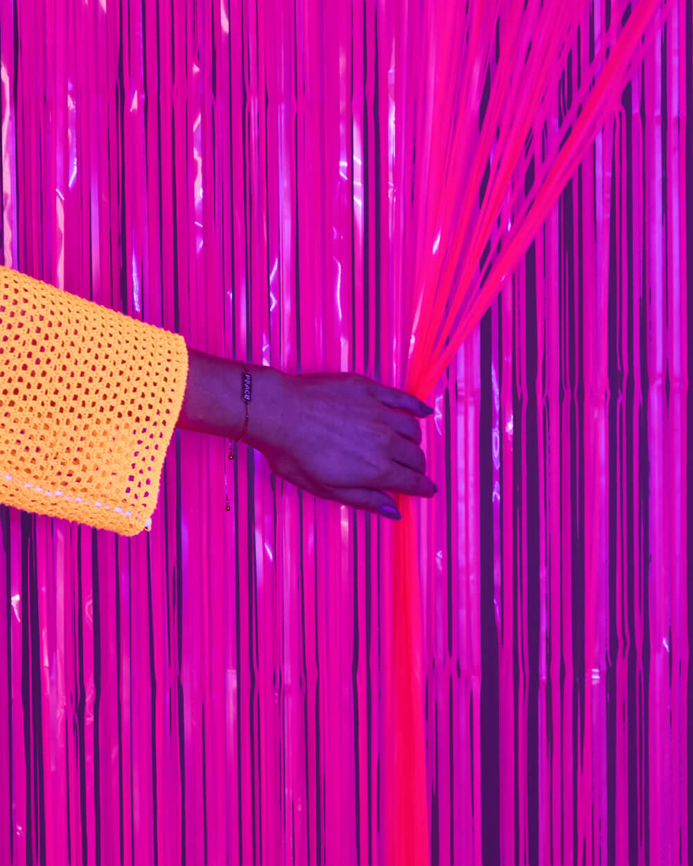 Hand parting the strands of a neon pink fringe curtain to show the layered magenta cut