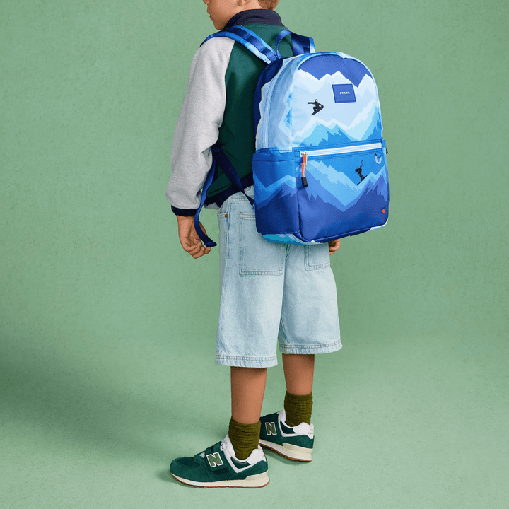 Boy in side profile wearing the blue Mountains Kane backpack against a green wall