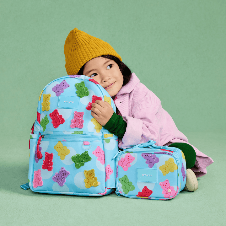 Child in a yellow beanie hugging the gummy bear backpack