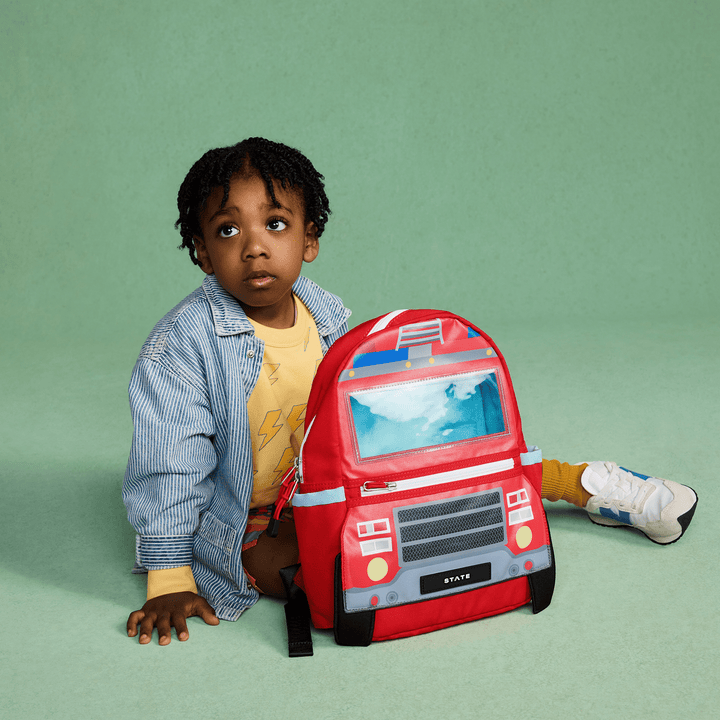 Toddler sitting on the floor beside the red fire truck backpack
