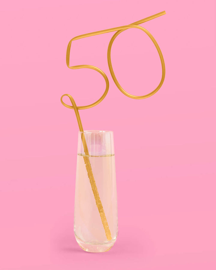 Gold 50 number straw standing in a glass of sparkling wine