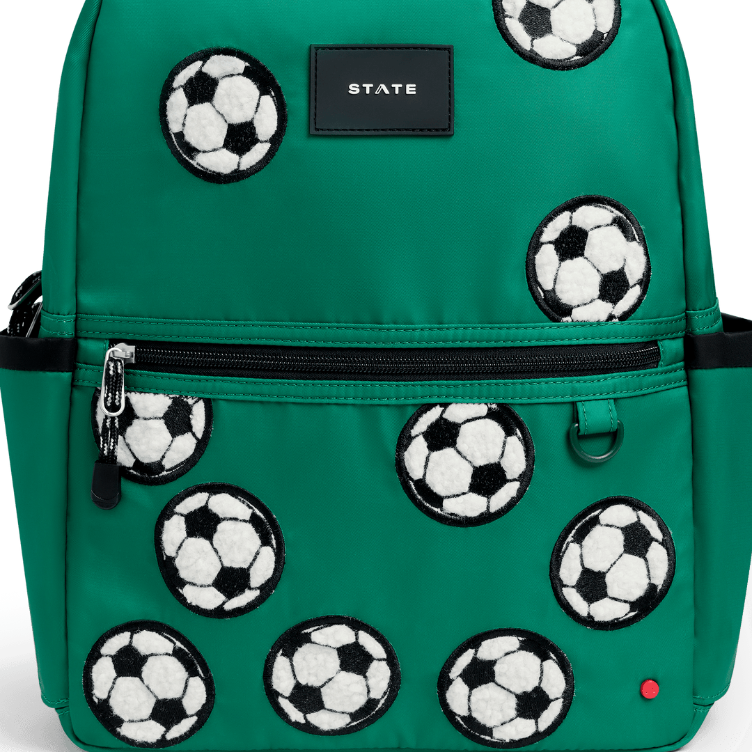 Close-up of the fuzzy soccer ball patches and STATE logo on the green Kane backpack