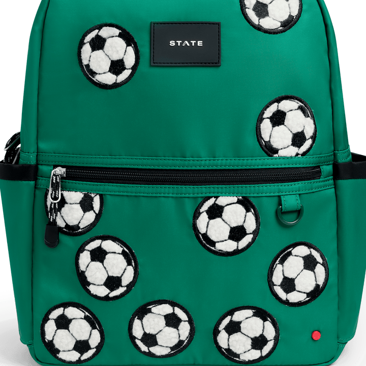 Close-up of the fuzzy soccer ball patches and STATE logo on the green Kane backpack