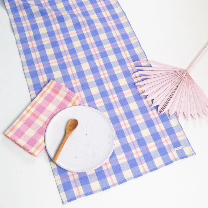 Periwinkle blue and pink plaid table runner across a styled table