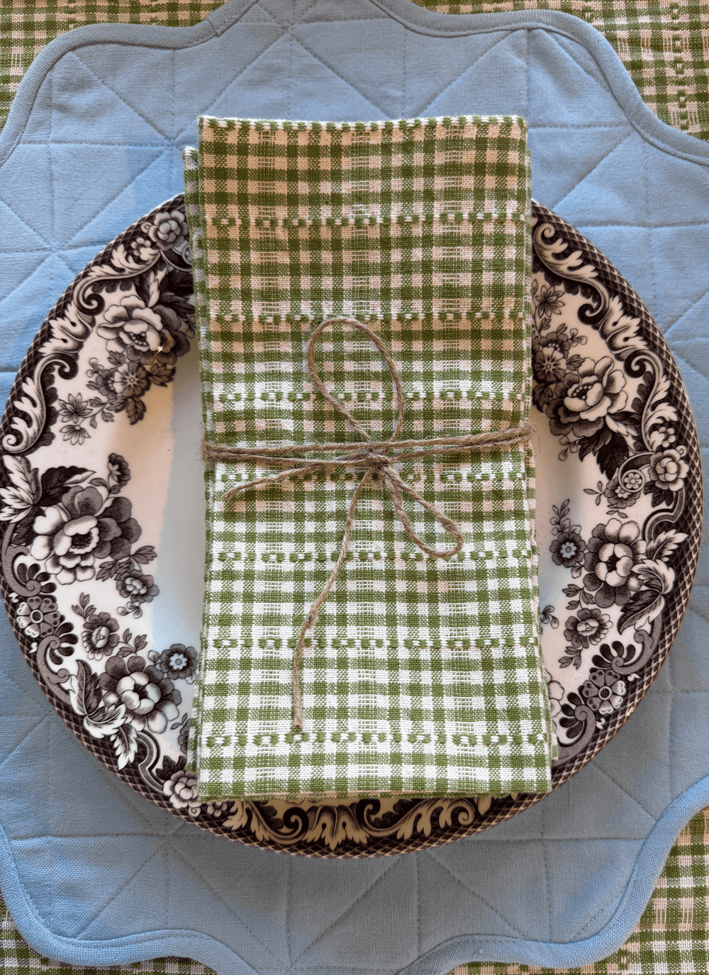 Green checkered napkin tied with twine on a decorative plate with floral pattern
