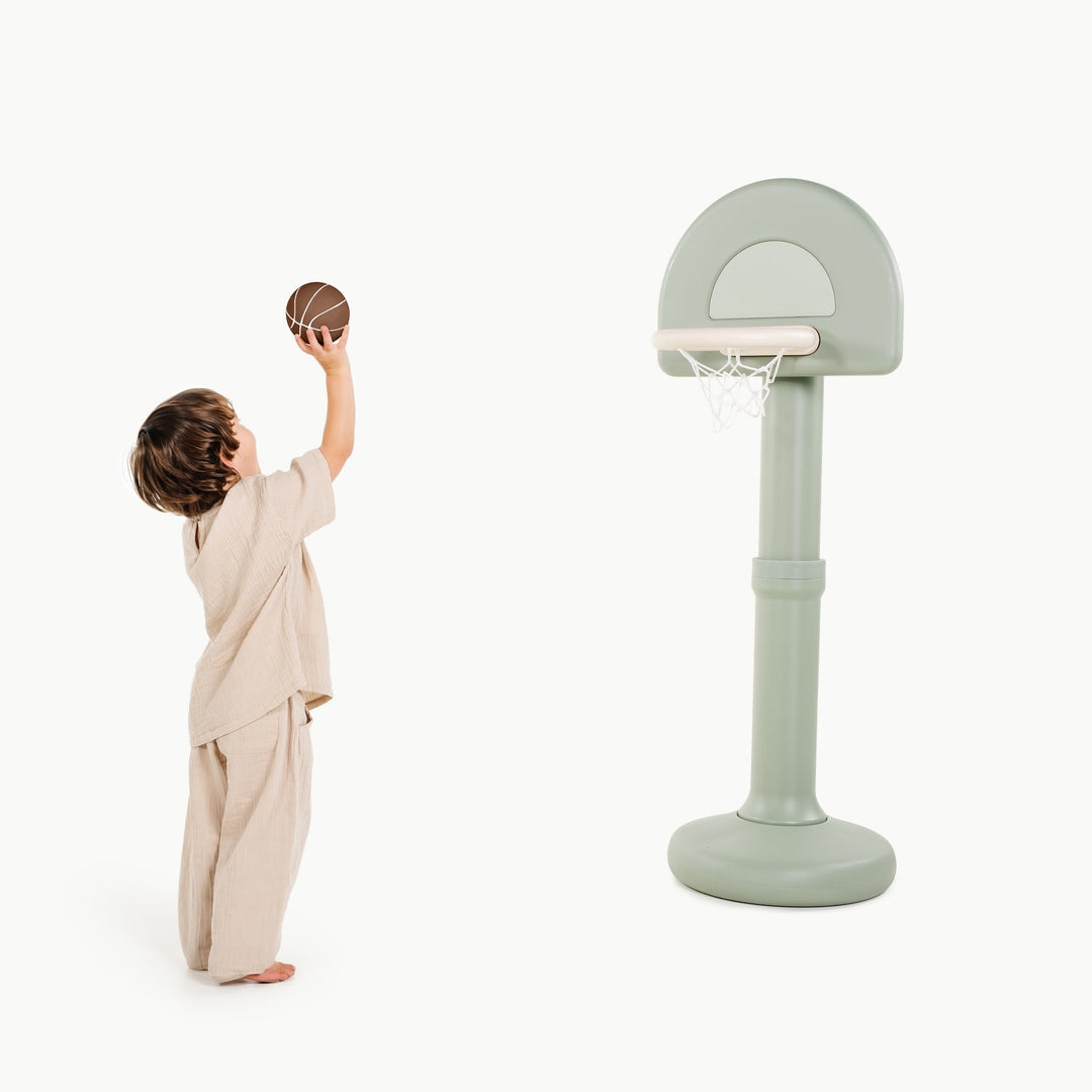 Boy tossing a basketball toward the palm green standing hoop, side view