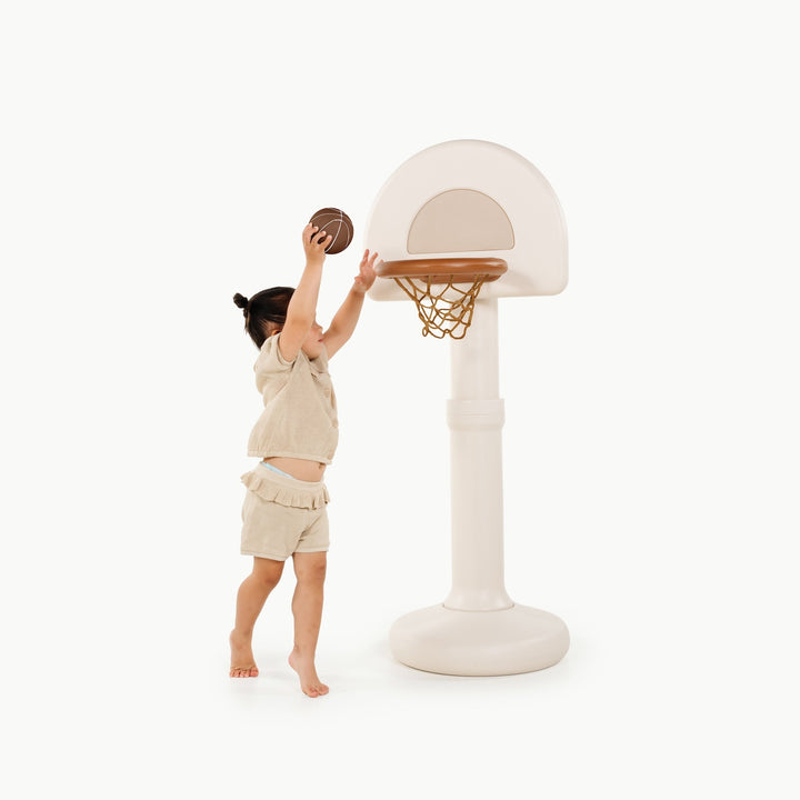 Little girl jumping to shoot a basketball at the ivory standing hoop