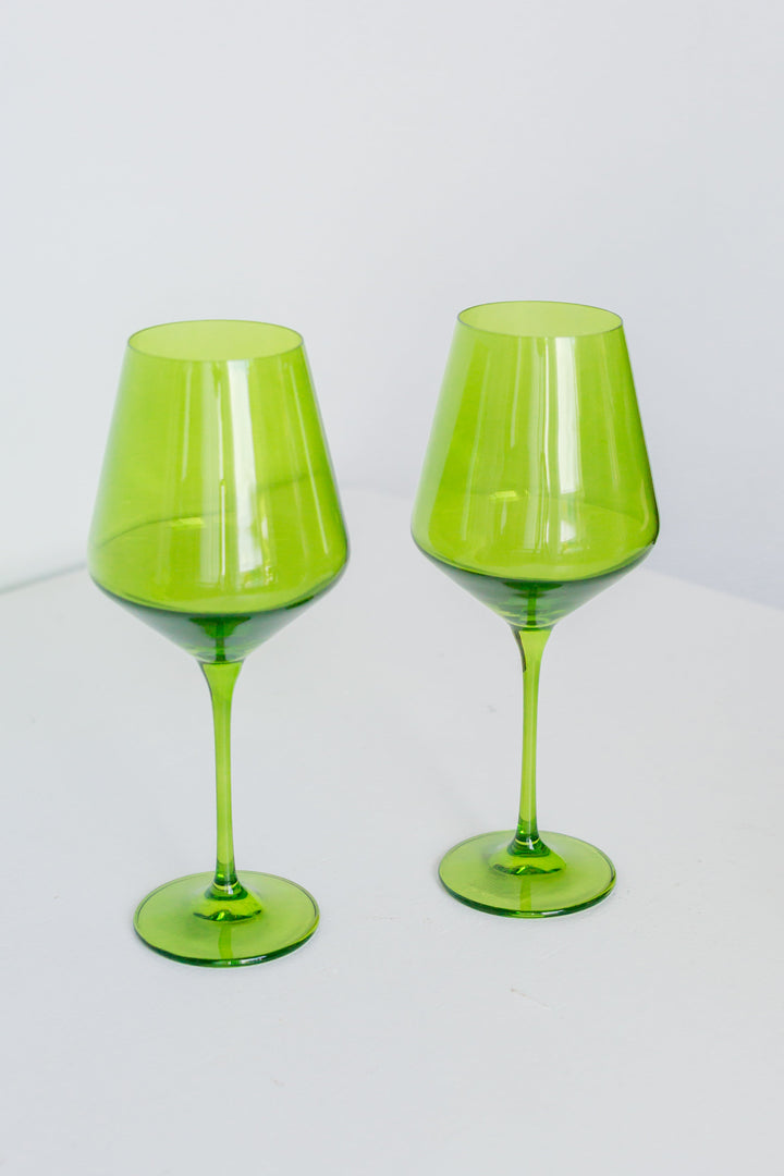 Two green wine glasses on a white surface with a white background