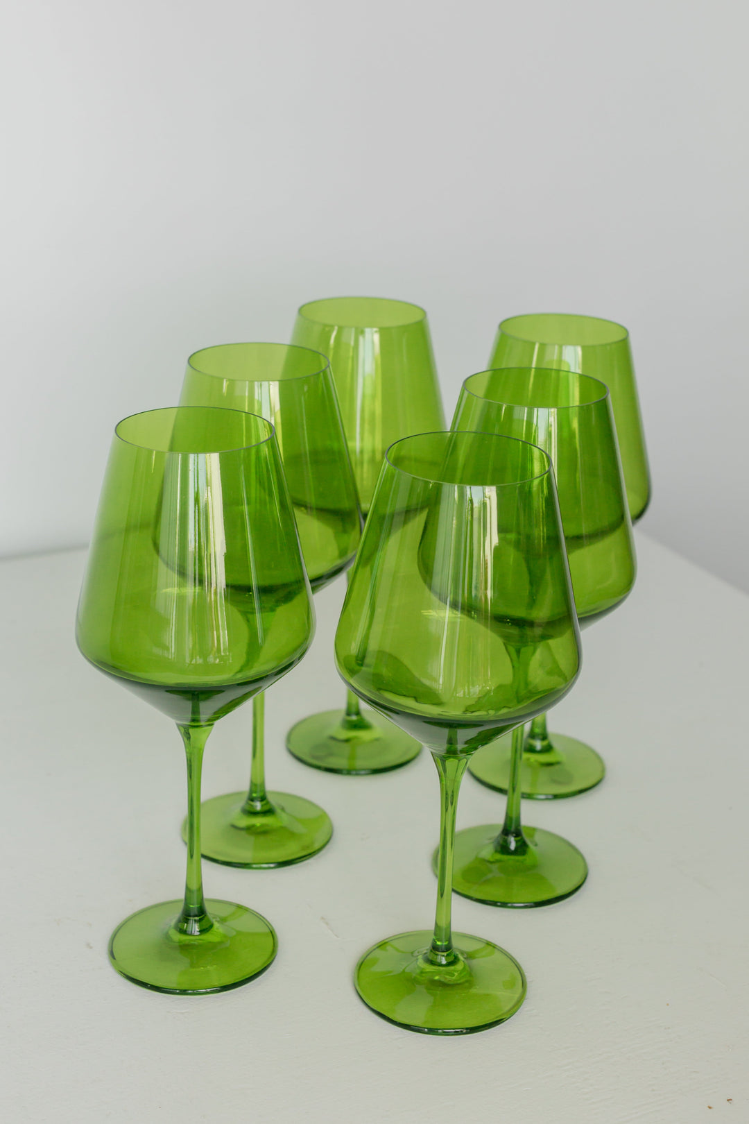 Six translucent green glass wine glasses arranged on a white surface against a light gray background.