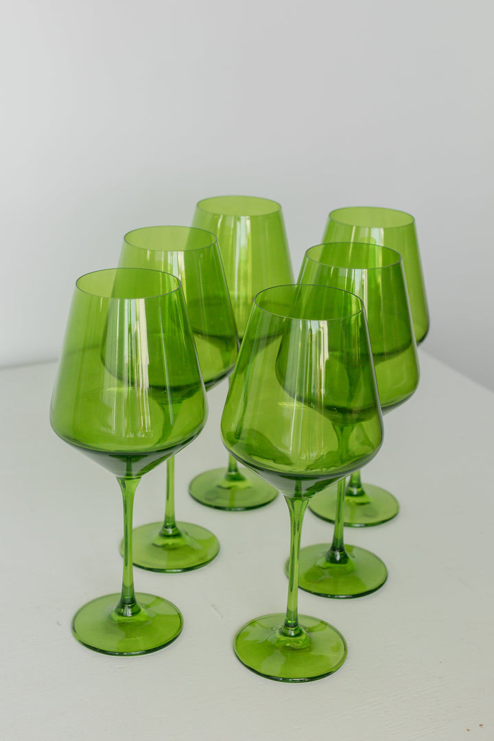 Six translucent green glass wine glasses arranged on a white surface against a light gray background.
