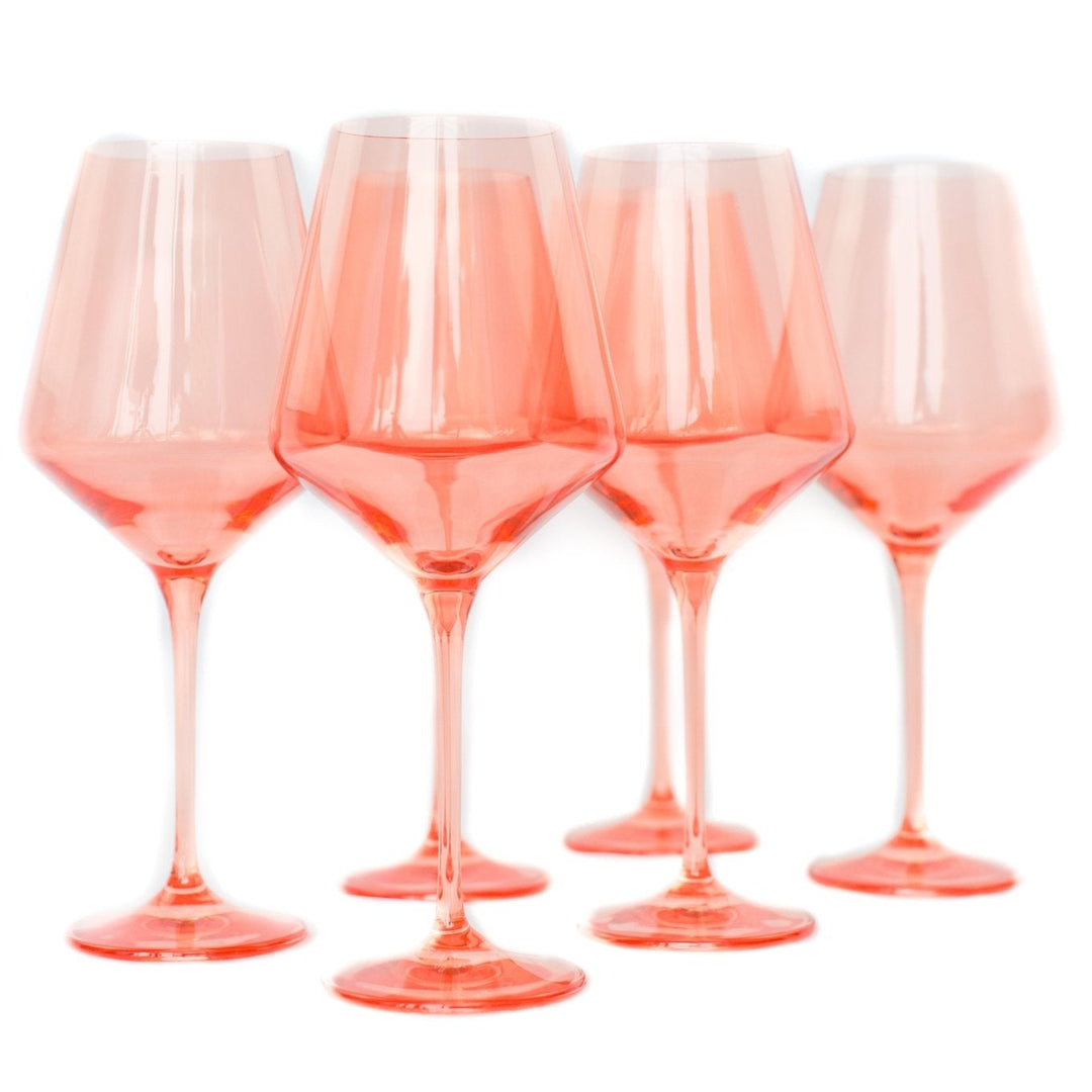 Estelle coral peach colored glass wine glasses grouped upright on a white backdrop, for a dinner party