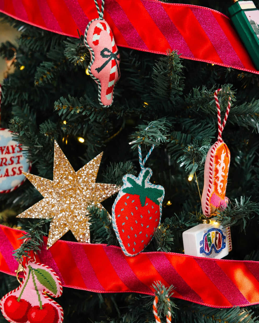 Strawberry ornament hanging on a tree with a gold star, pink ribbon, and other Furbish ornaments