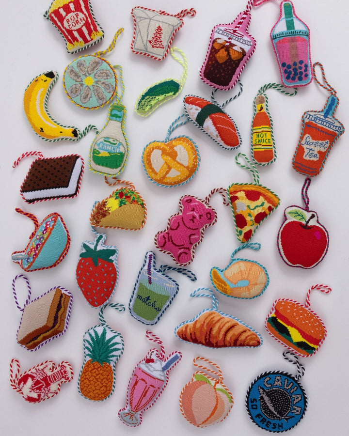 Flat lay of Furbish food needlepoint ornaments on white, the peach near the bottom