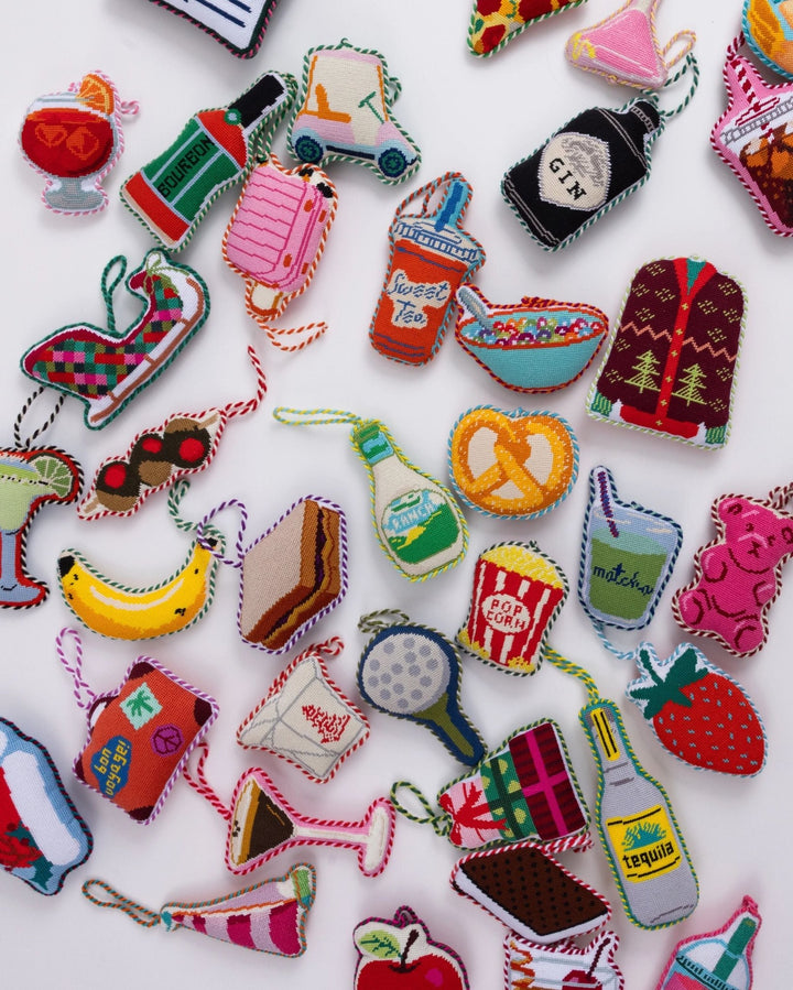 Flat lay of many Furbish icon needlepoint ornaments, the striped sailboat near the bottom