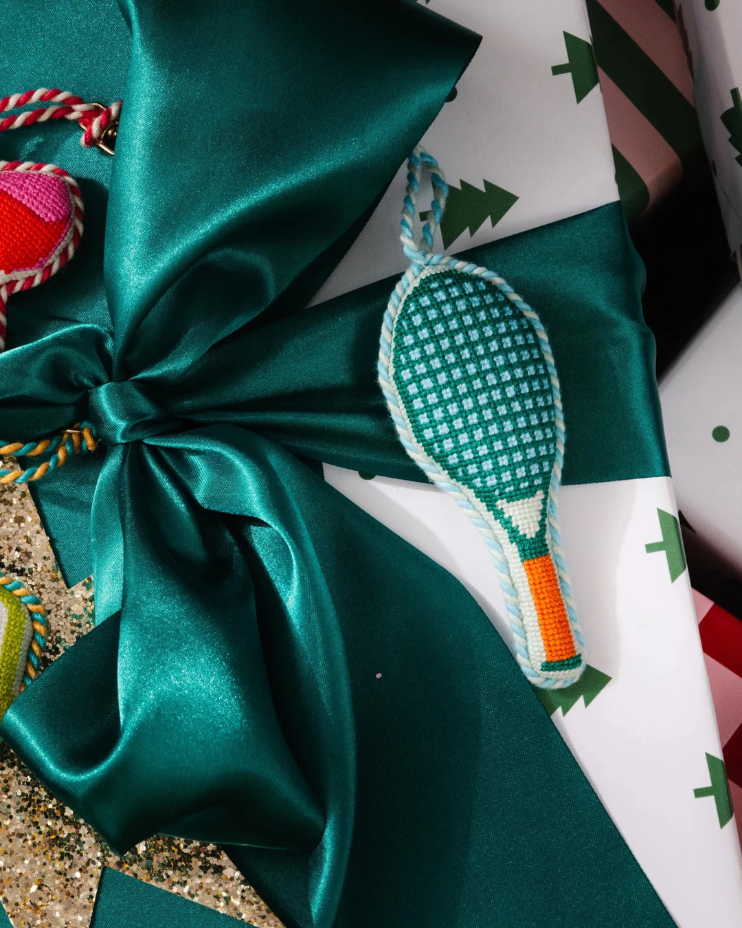 Tennis racket ornament laid on a green satin bow over a white Christmas tree print gift