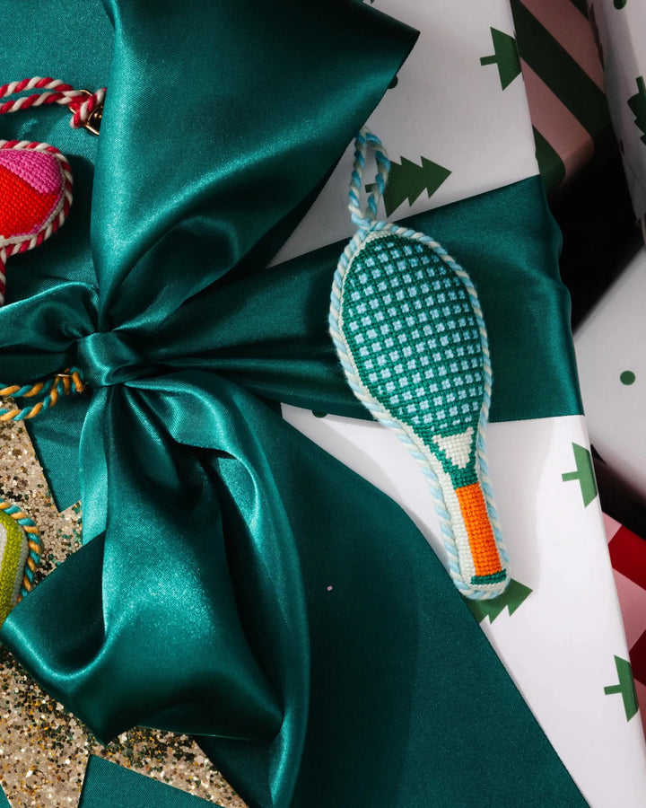 Tennis racket ornament laid on a green satin bow over a white Christmas tree print gift