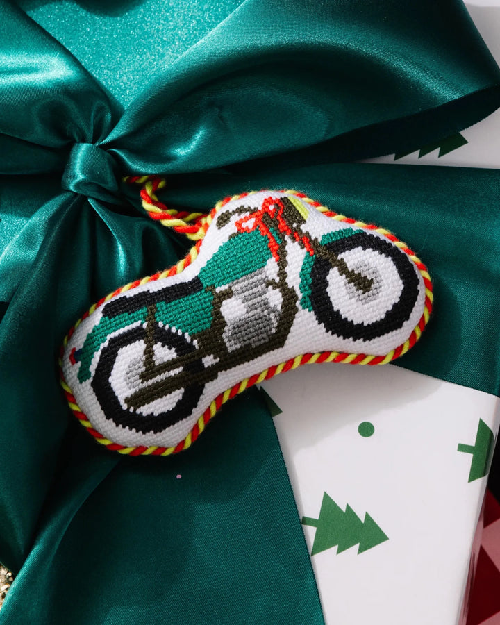 Motorcycle ornament resting on a green satin bow over tree print wrapping paper