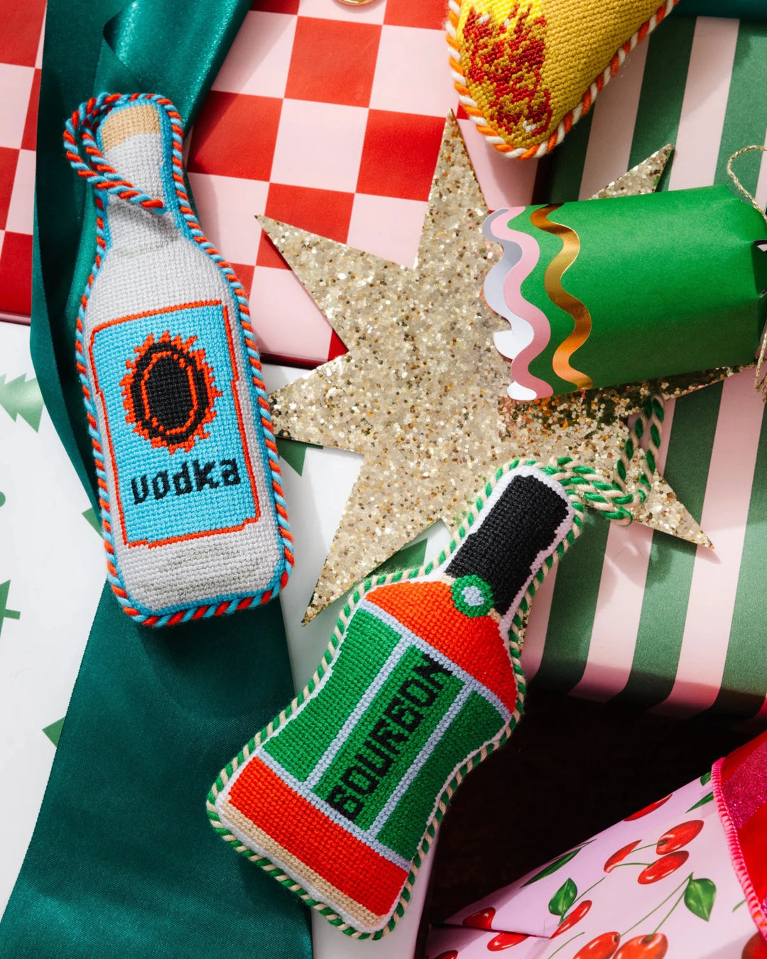 Vodka bottle ornament on festive wrapping with a gold star and a green bourbon bottle ornament