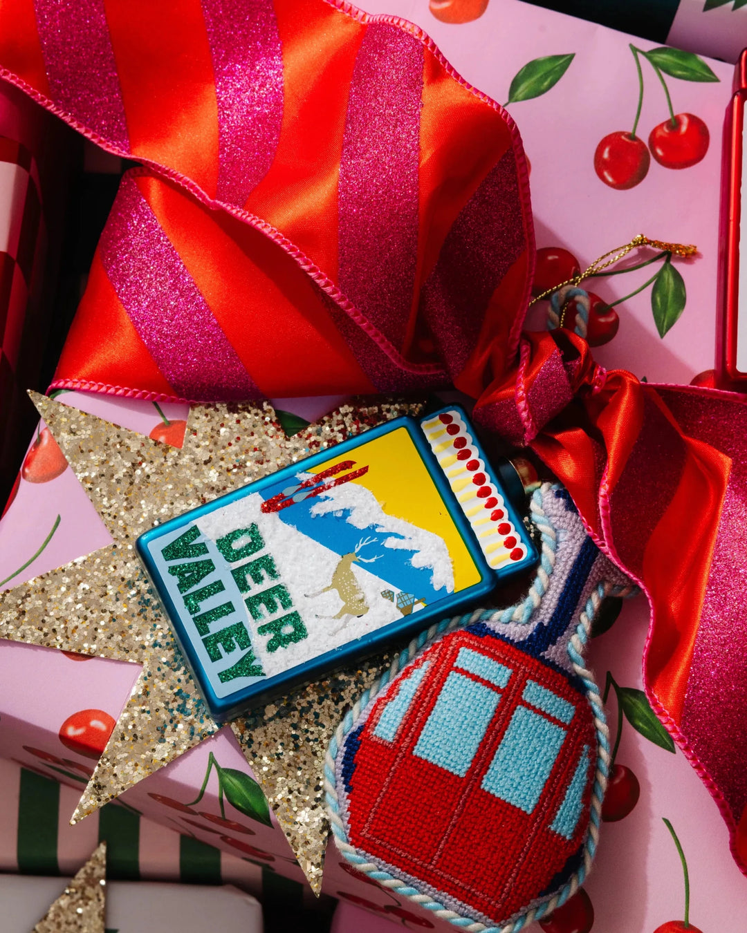 Gondola ornament on a pink cherry print gift beside a Deer Valley needlepoint ornament