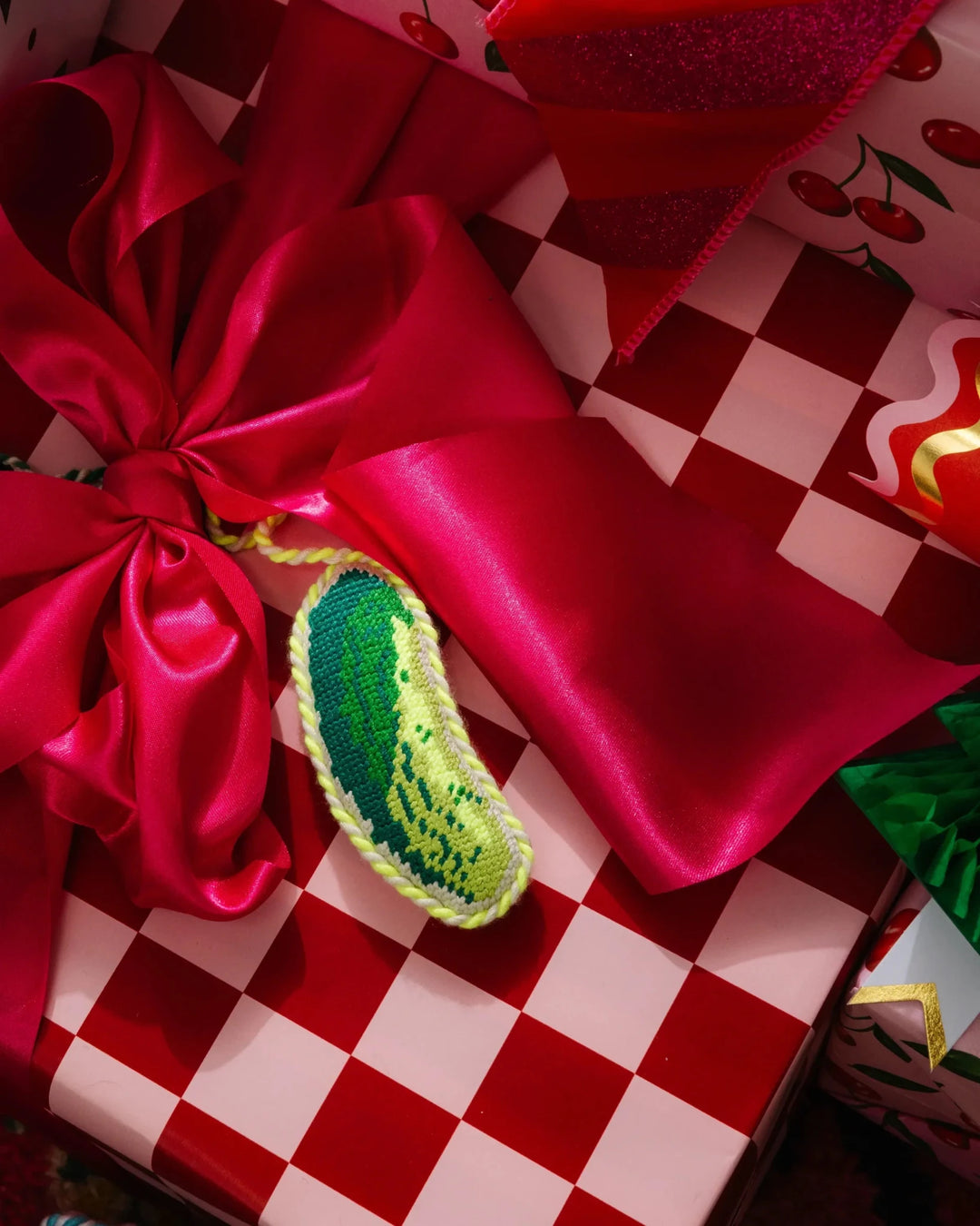 Pickle ornament on a red and pink checkered gift with a magenta satin bow