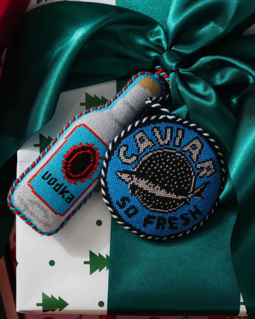 Vodka bottle ornament on a green satin bow beside a round Caviar So Fresh needlepoint ornament