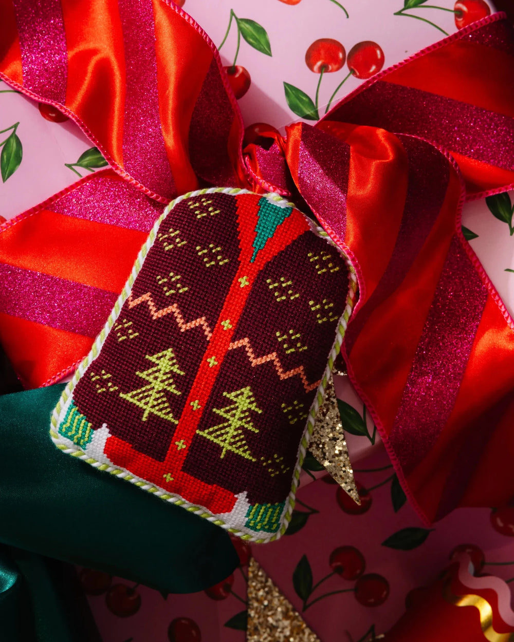 Christmas sweater ornament resting on a red satin bow over cherry print wrapping paper