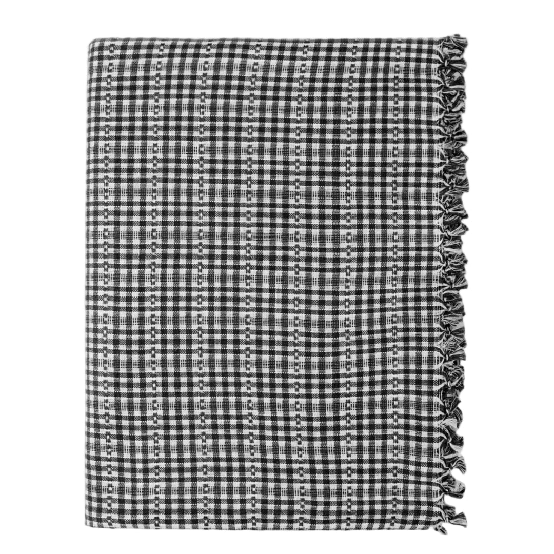 A folded black and white checkered scarf with vertical rows of small white dots and fringed edges, shown on a light gray background.