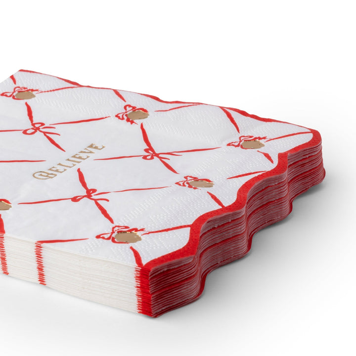 Stack of Polar Express Believe napkins with a red ribbon lattice and gold bells for a Christmas party