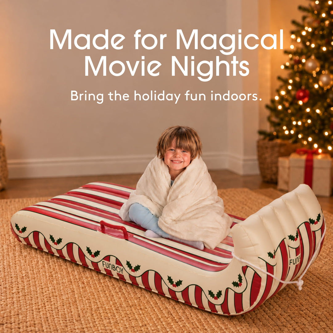 Child wrapped in a blanket in a holly stripe inflatable sled beside a Christmas tree
