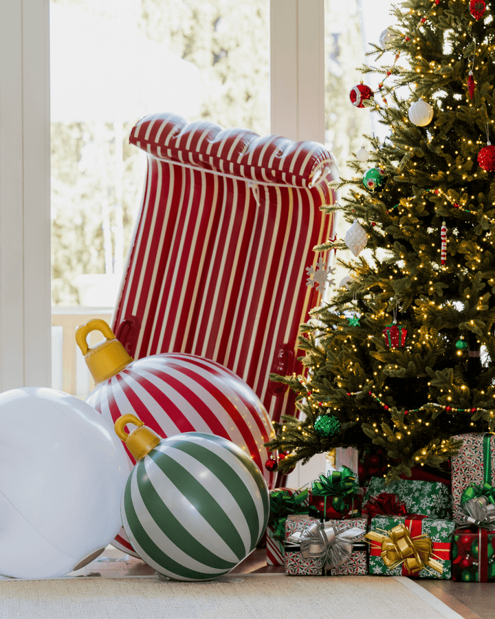 Red and white inflatable toboggan standing by a Christmas tree with giant inflatable ornaments