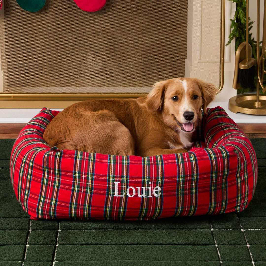 Dog curled in the tartan bolster bed in a cozy room with red and green ornaments above