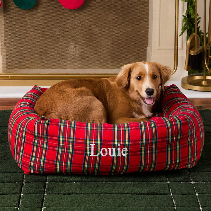 Dog curled in the tartan bolster bed in a cozy room with red and green ornaments above
