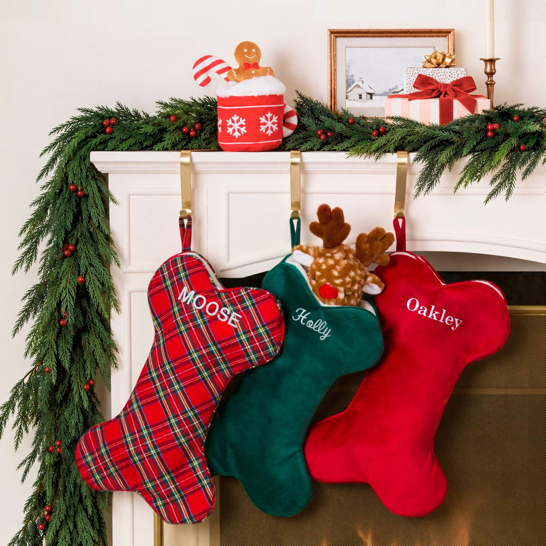 Tartan, green velvet, and cranberry velvet dog stockings hung on a garland mantel with toys peeking out